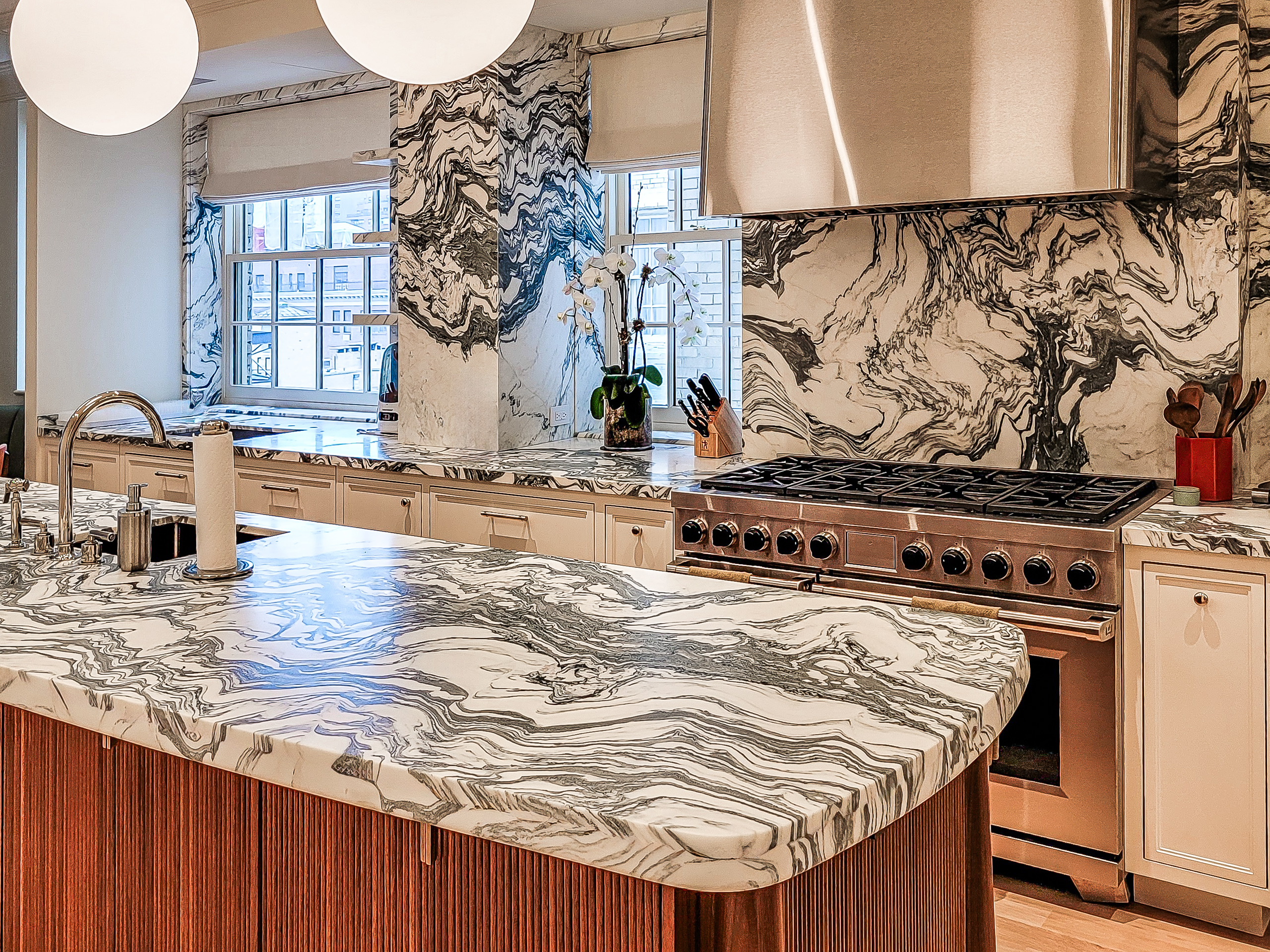 Arni Fantastico marble island with a custom rounded edge and matching full-height backsplash behind the range.