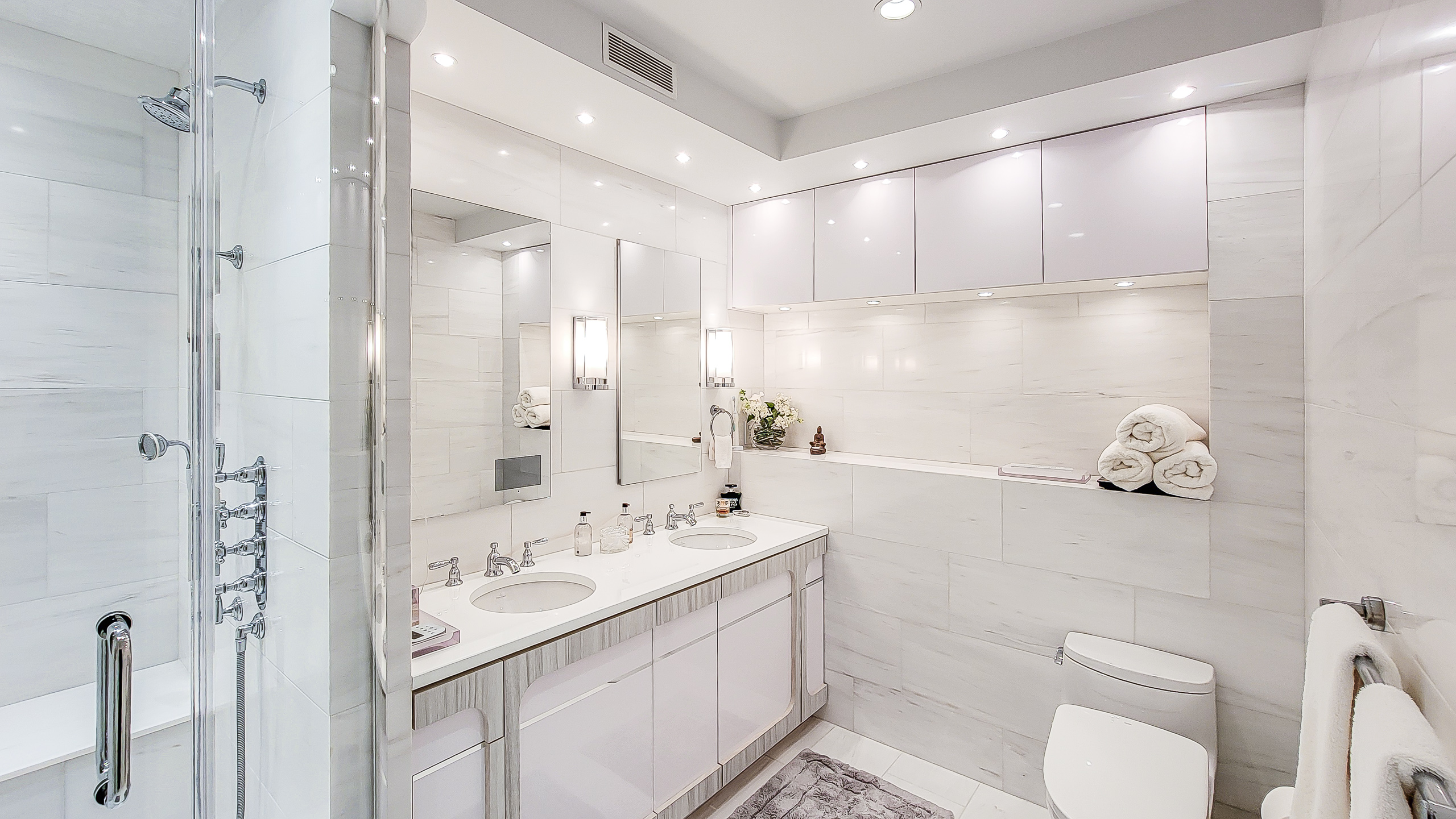 Bianco Dolomiti wall tiles surrounding a glass-enclosed shower and double vanity in a white bathroom.