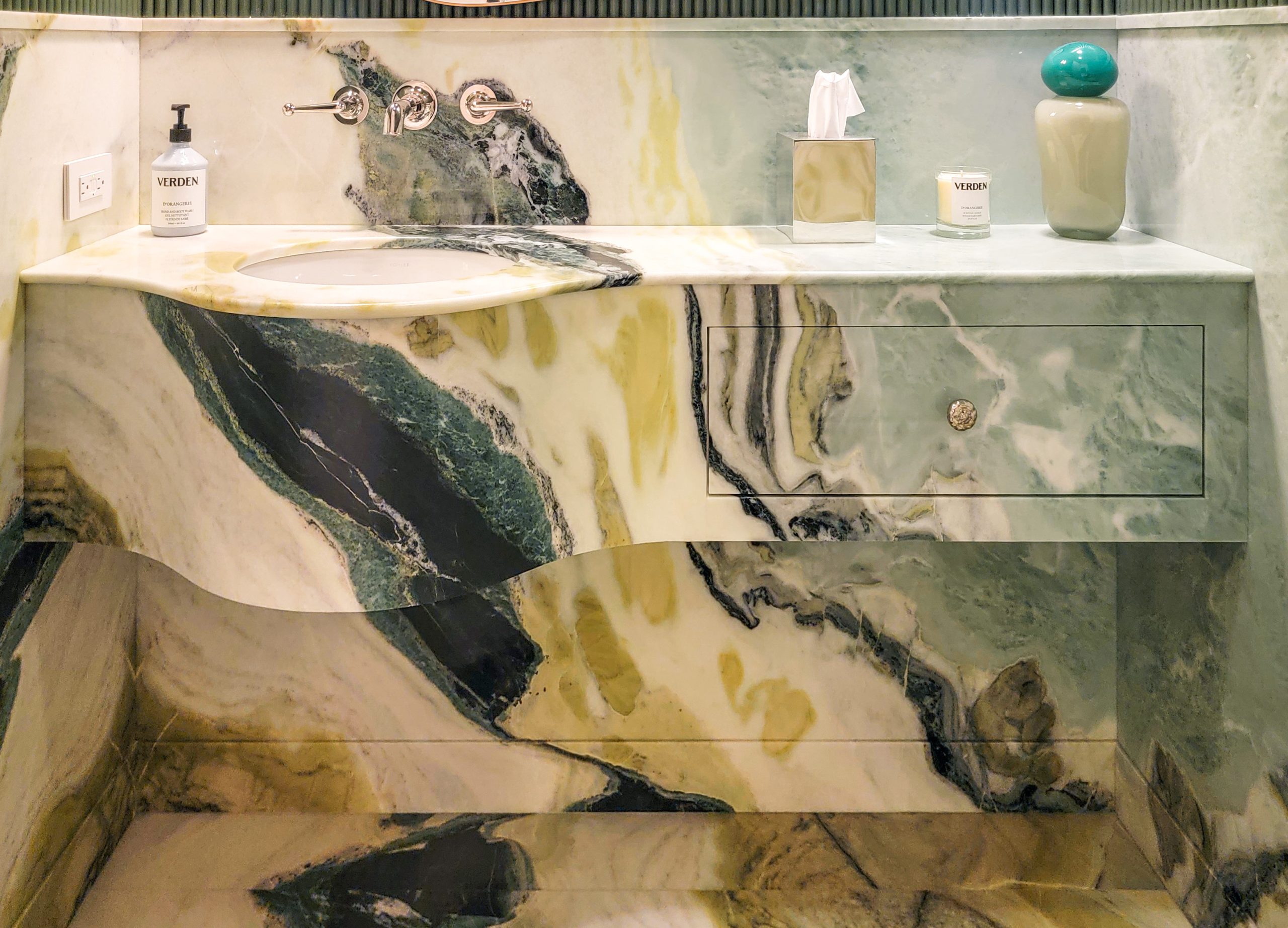 Dreaming Green marble vanity with a curved front, stone drawer face, undermount basin, and matching backsplash.