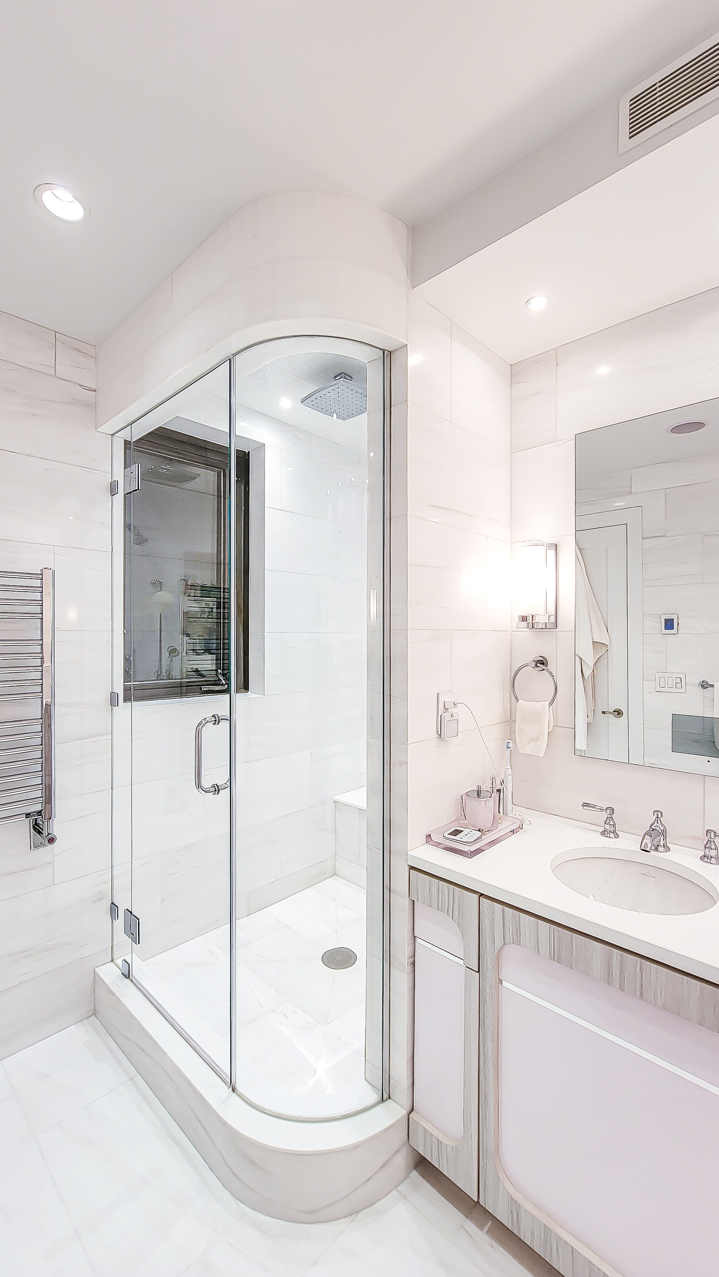 Curved glass shower enclosure with white stone tile, a window, and an adjacent vanity.