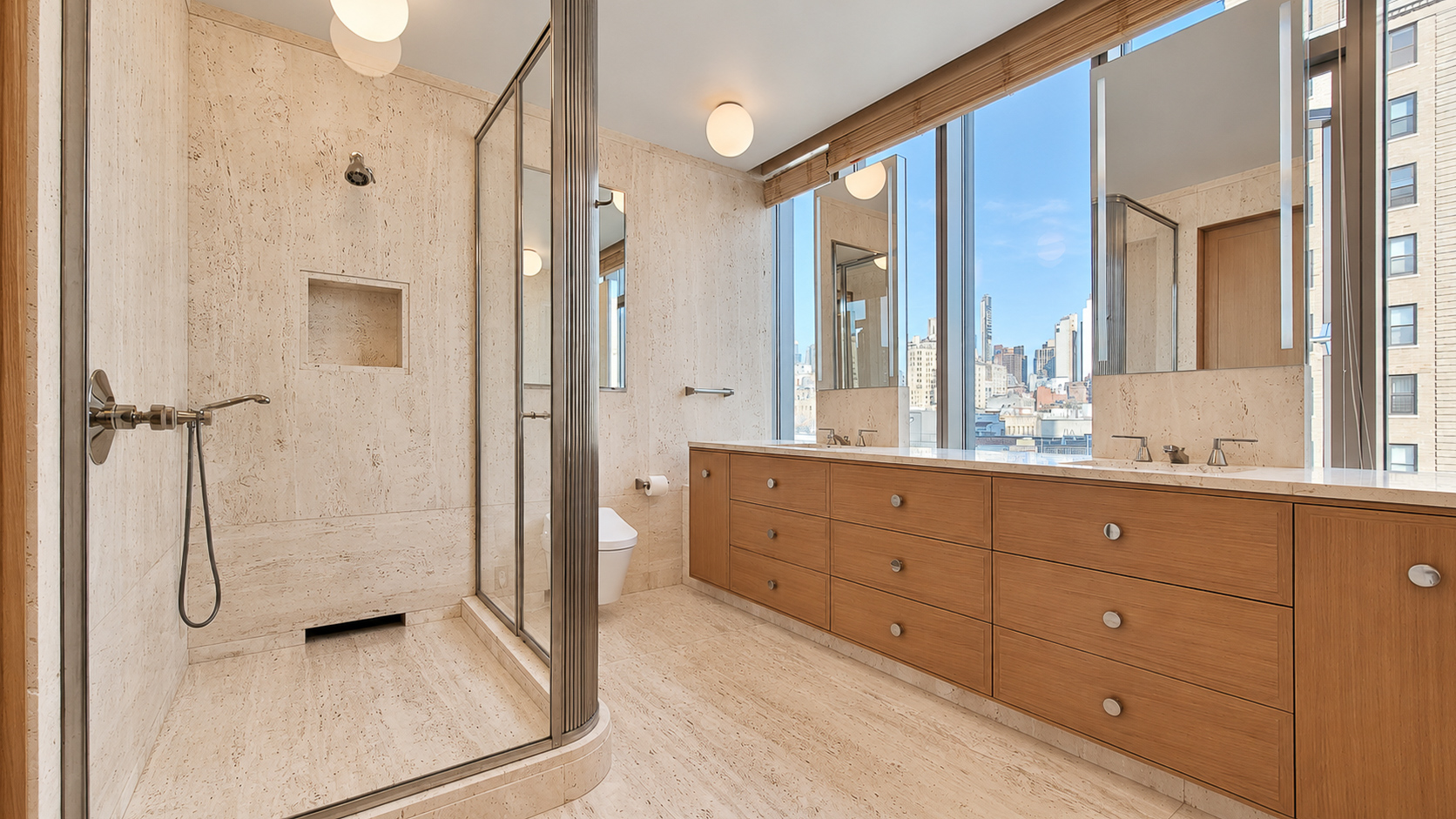 Wide bathroom view with a travertine shower beside the long wood vanity