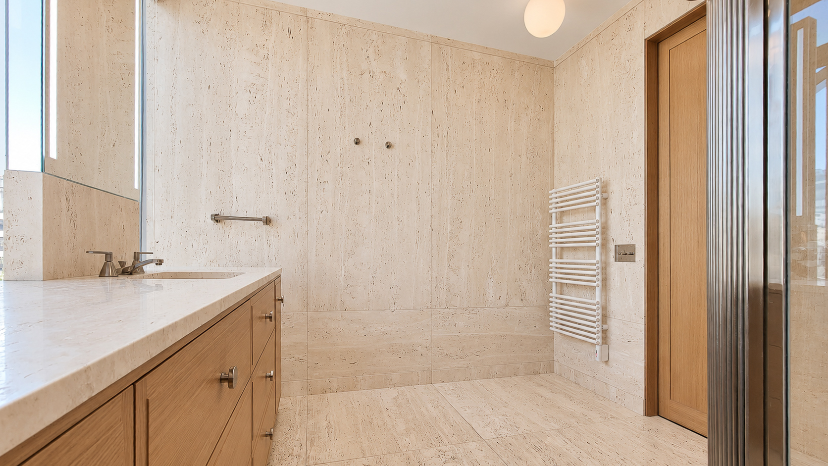 Travertine bathroom walls and floor beside a wood doorway and towel radiator