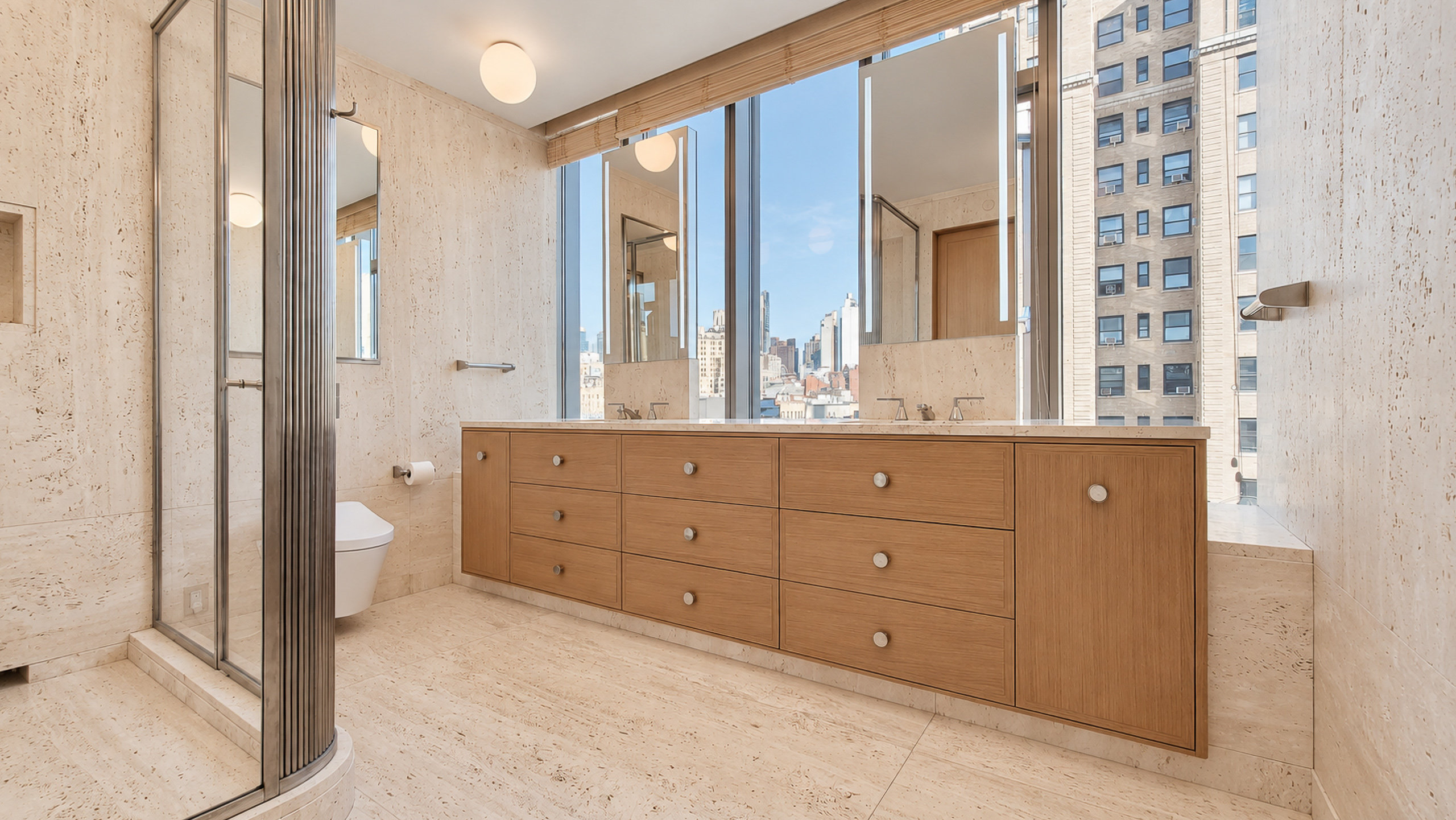 Navona travertine bathroom with a wood double vanity, curved glass shower and city-facing windows